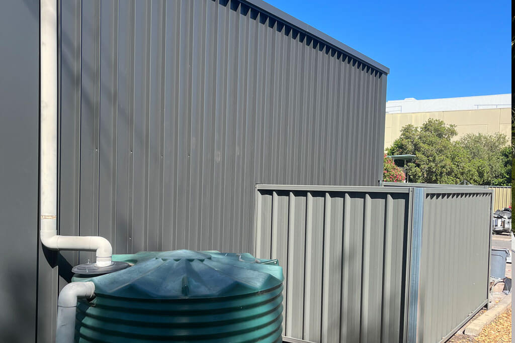 Grey Metal Wall Cladding with open grey metal box and green metal circle that connected through with white downpipes